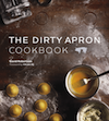 Book cover of the Dirty Apron Cookbook. The cover shows a countertop with some pieces of freshly made uncooked ravioli and a bowl of egg wash.