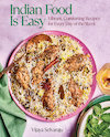 A pink plate seen from above on a pinkish-purple background. The plate is filled with long-grain rice, pieces of chicken, and spices, with a copper spoon lying on it. A green napkin lies on the left side, and part of a plate of mint leaves and small dish of sauce are on the right.'